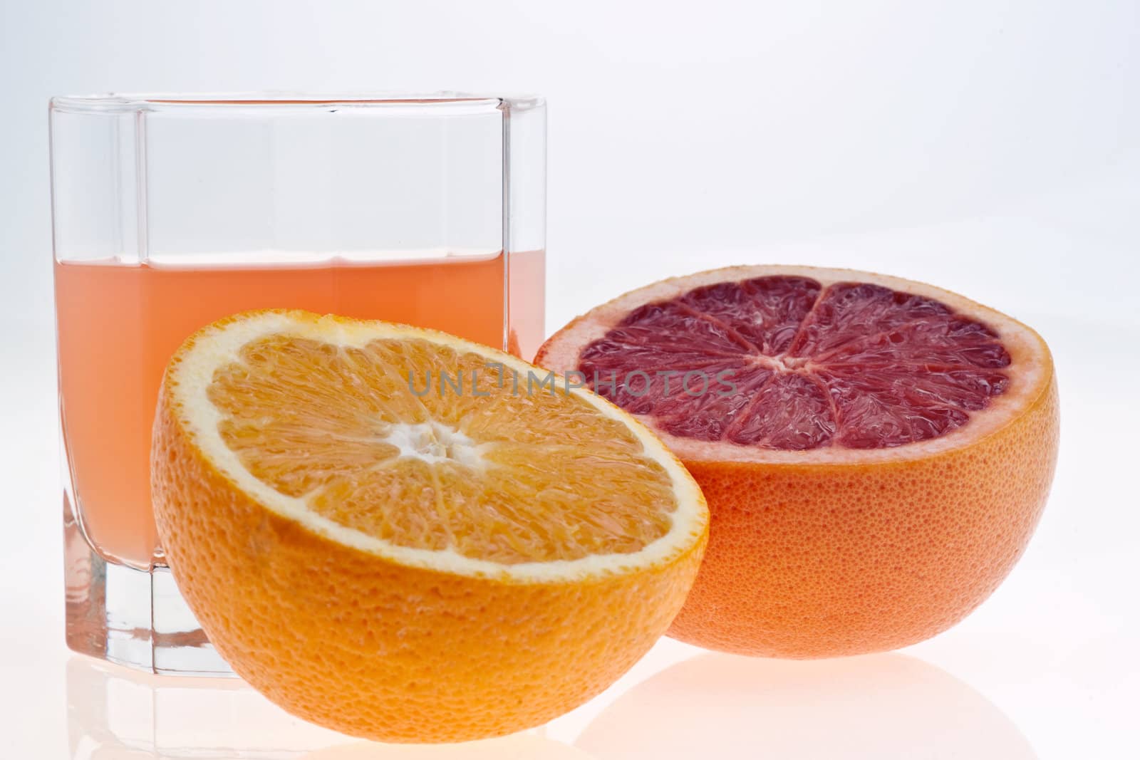 two halves of grapefruit and juice in glass on white
