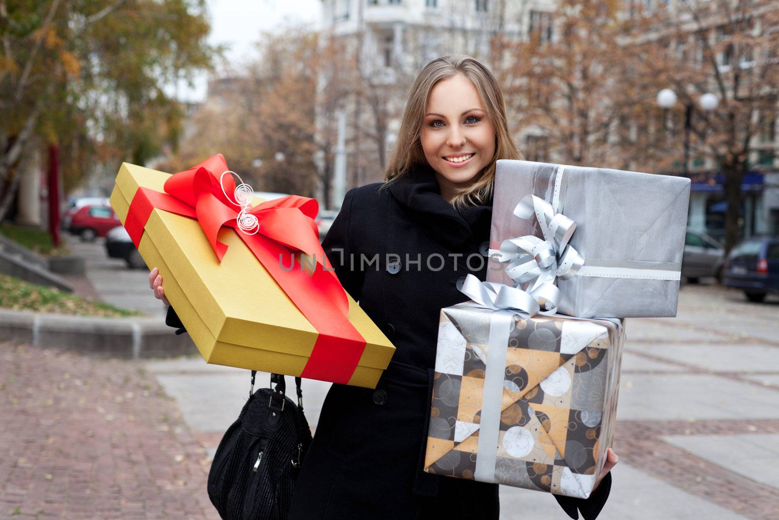 Beautiful smiling woman in the street holding presents, looking at camera