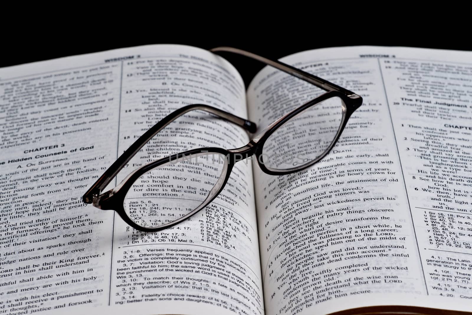 Open bible and the glasses on black background