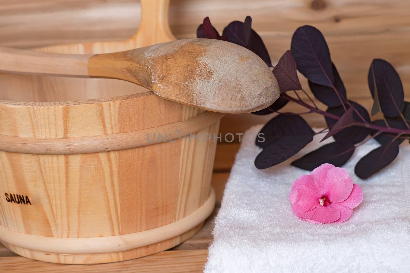 bucket with ladle across it next to towel with flowers inside a sauna