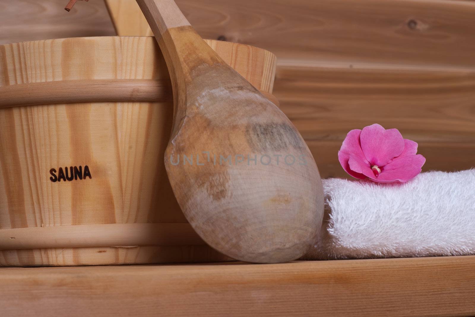 white towel with flower on top next to bucket with ladle in a wooden sauna
