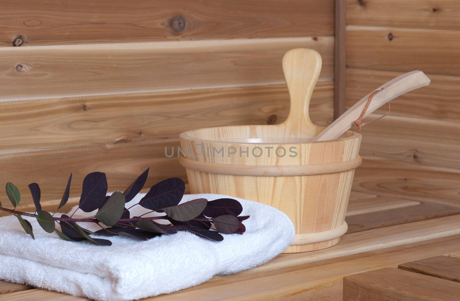 wooden sauna with bucket and ladle beside towel and flower