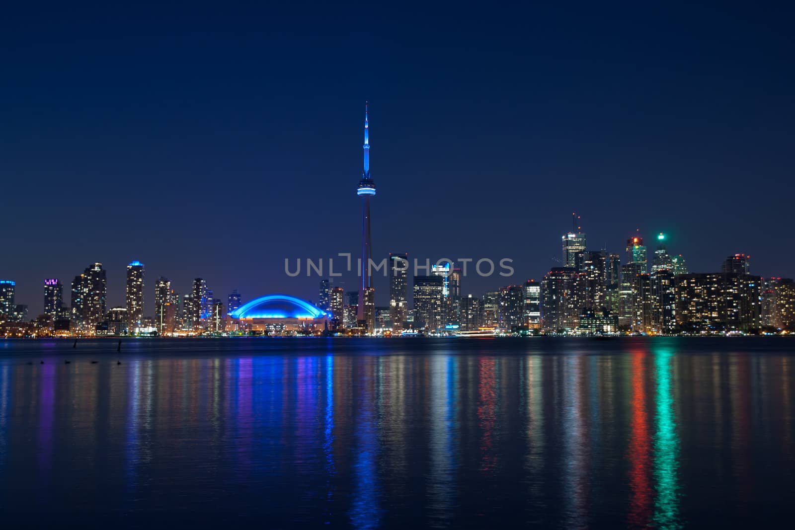 The landmark Toronto downtown view from the center island. Scenic view of the Tower illuminated by the iconic downtown skyline of skyscrapers and high rise condominiums reflecting in Lake Ontario 