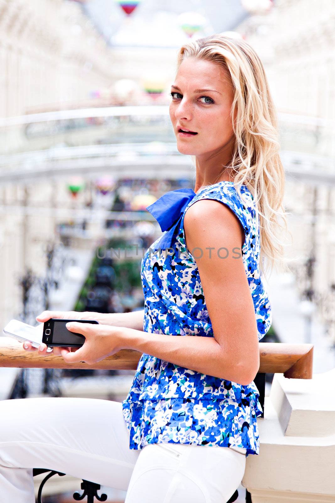 Young and beautiful woman with blond hair is on the phone at the mall