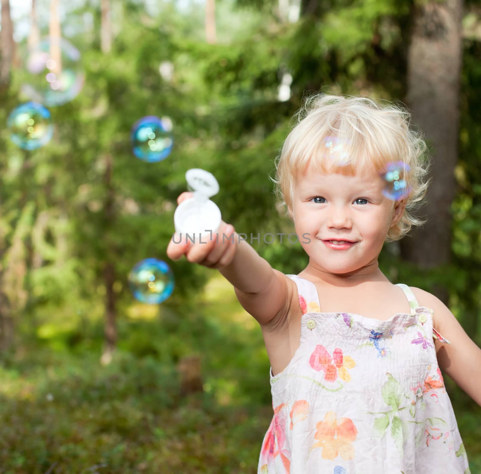 Cute little girl playing with soap bubbles outdoors