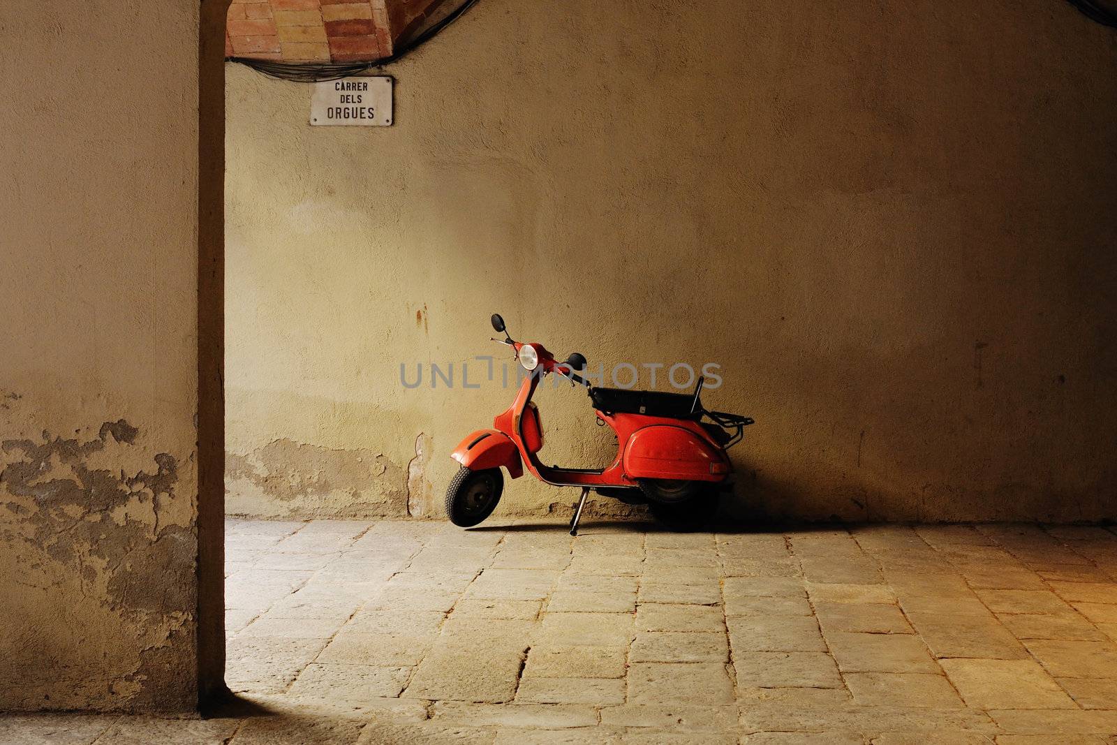 small red motorbike parked at medieval cobblestone yard in Barcelona Spain