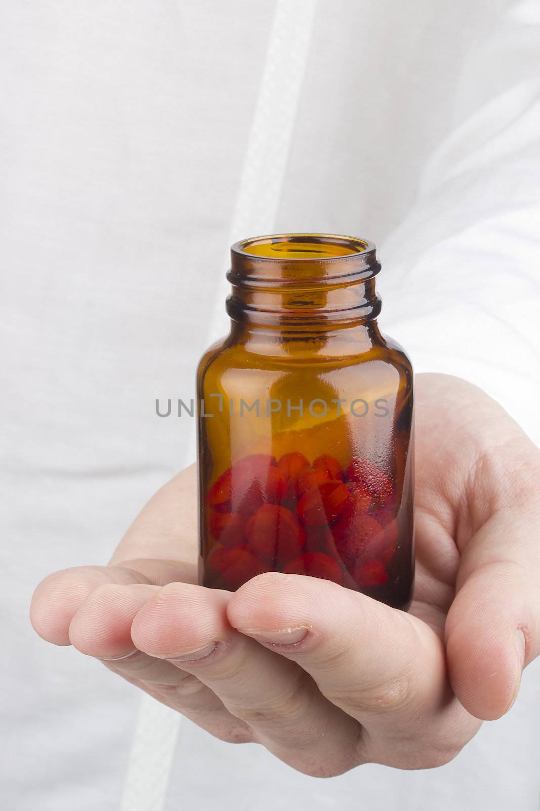 Close-up photograph of a hand holding a transparent glass container with red tablets.