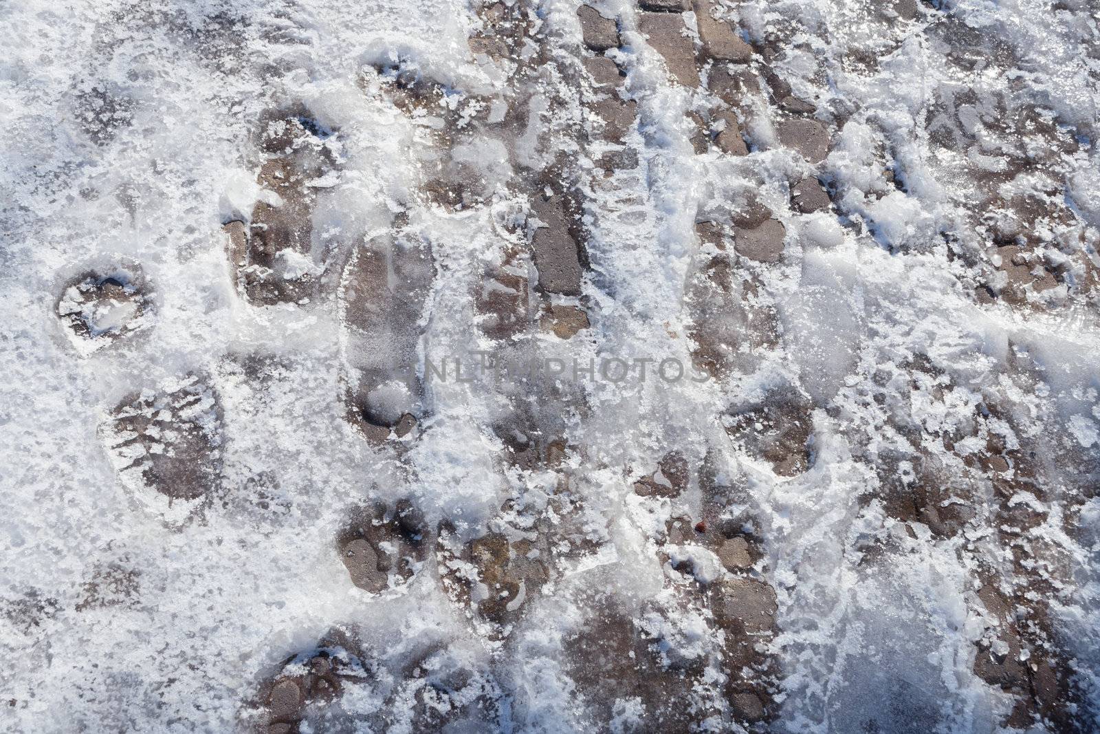 many soles prints frozen on pavement in snow and ice mixture