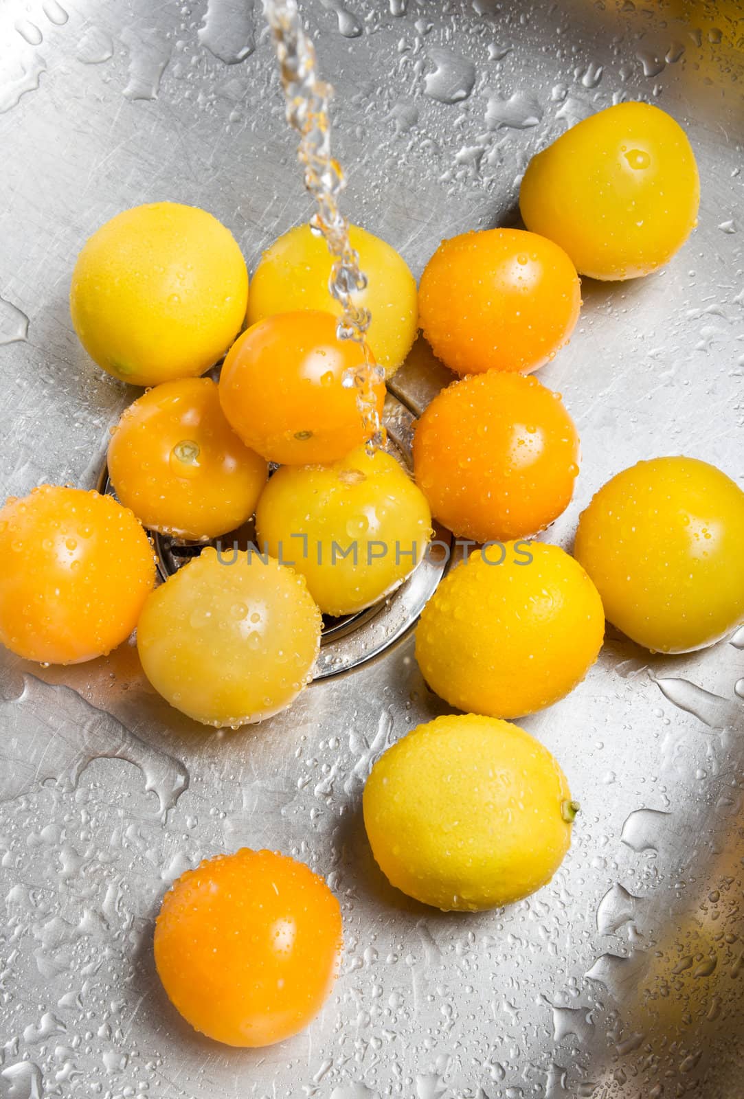 Washing yellow tomatoes and lemons in the kitchen sink.