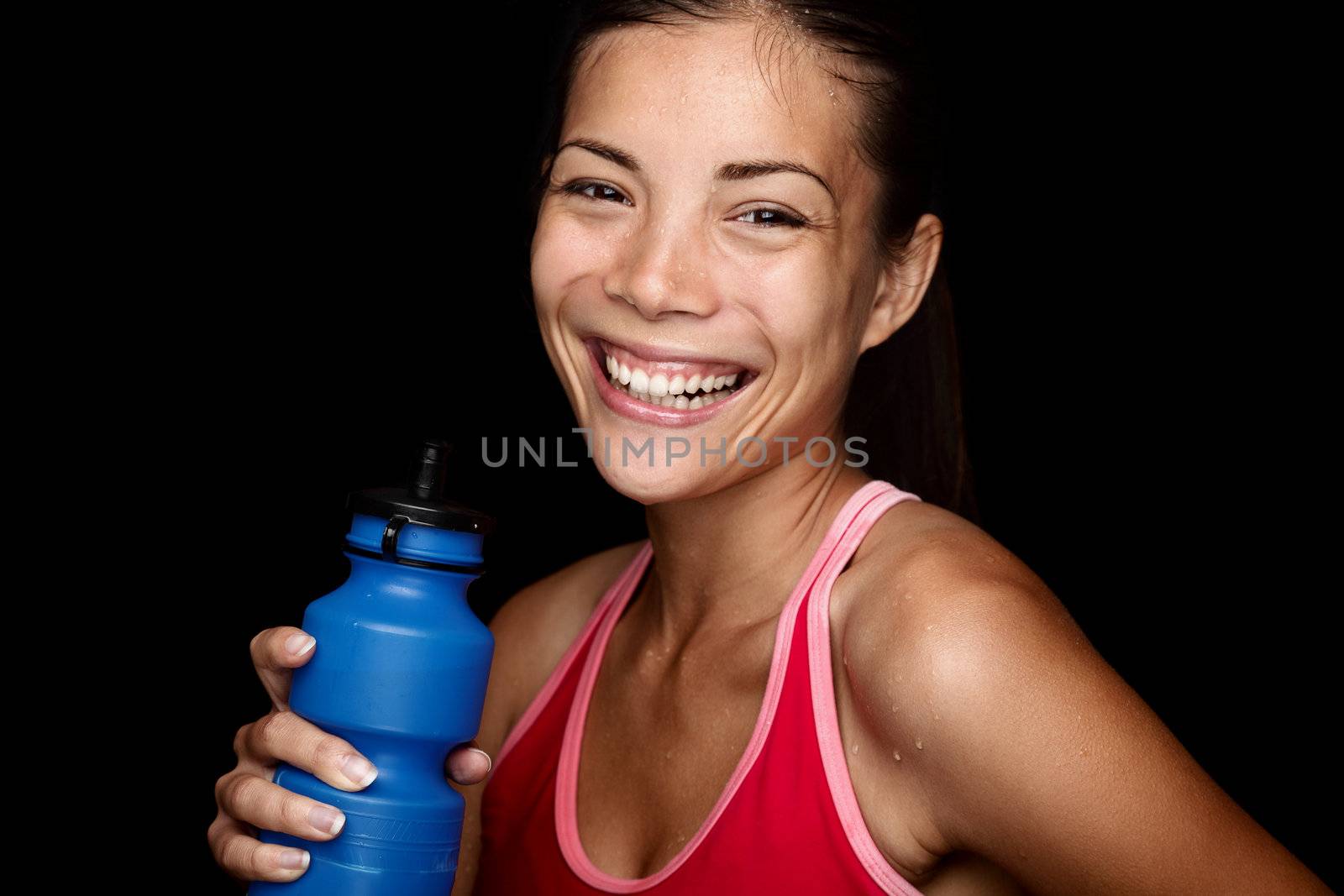Smiling fitness sportswoman with a blue sport bottle on black background. Multiracial Asian fitness model happy.