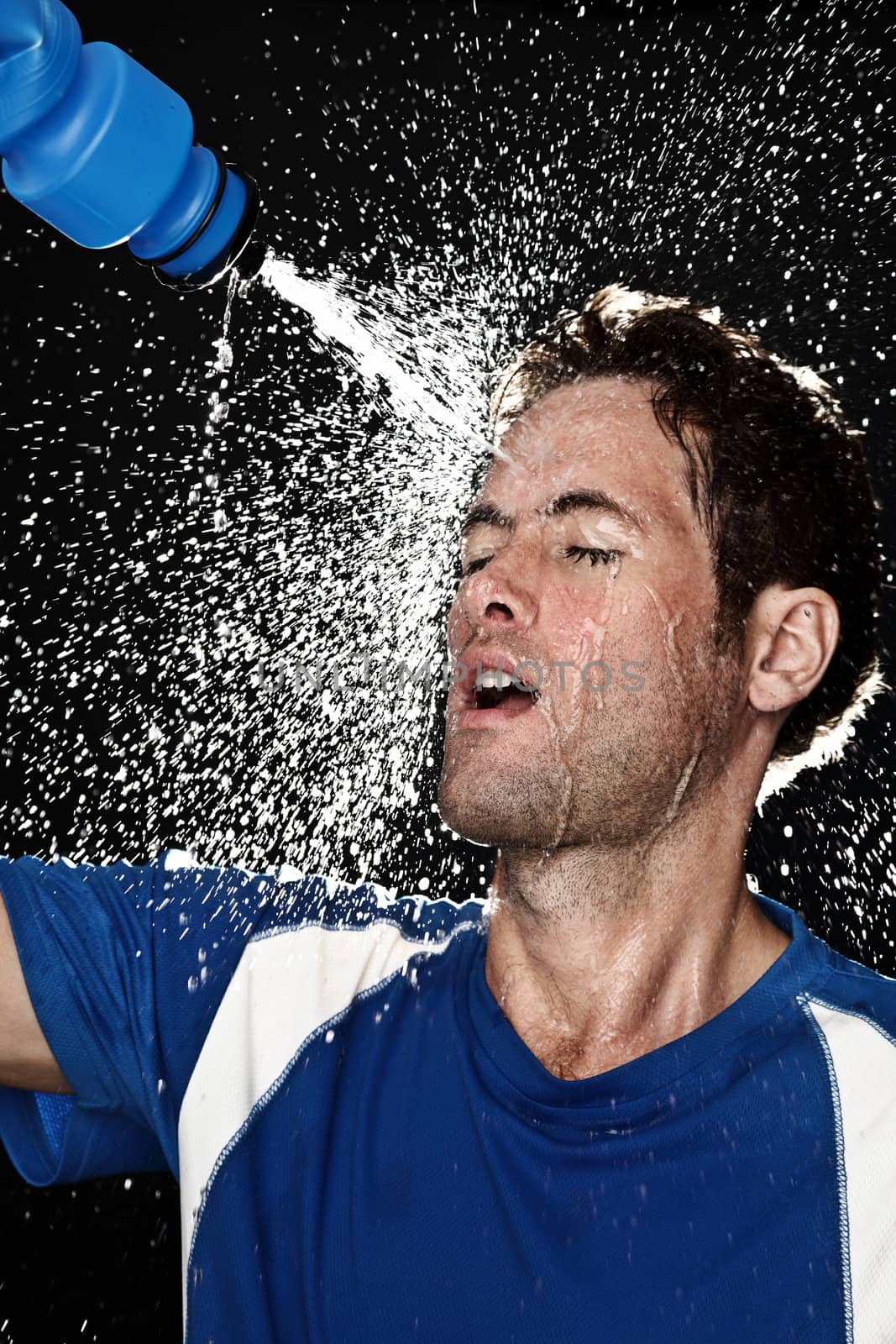 Sport fitness man. Studio shot of a young athletic man cooling himself after training by squirting water over himself from a drinks bottle