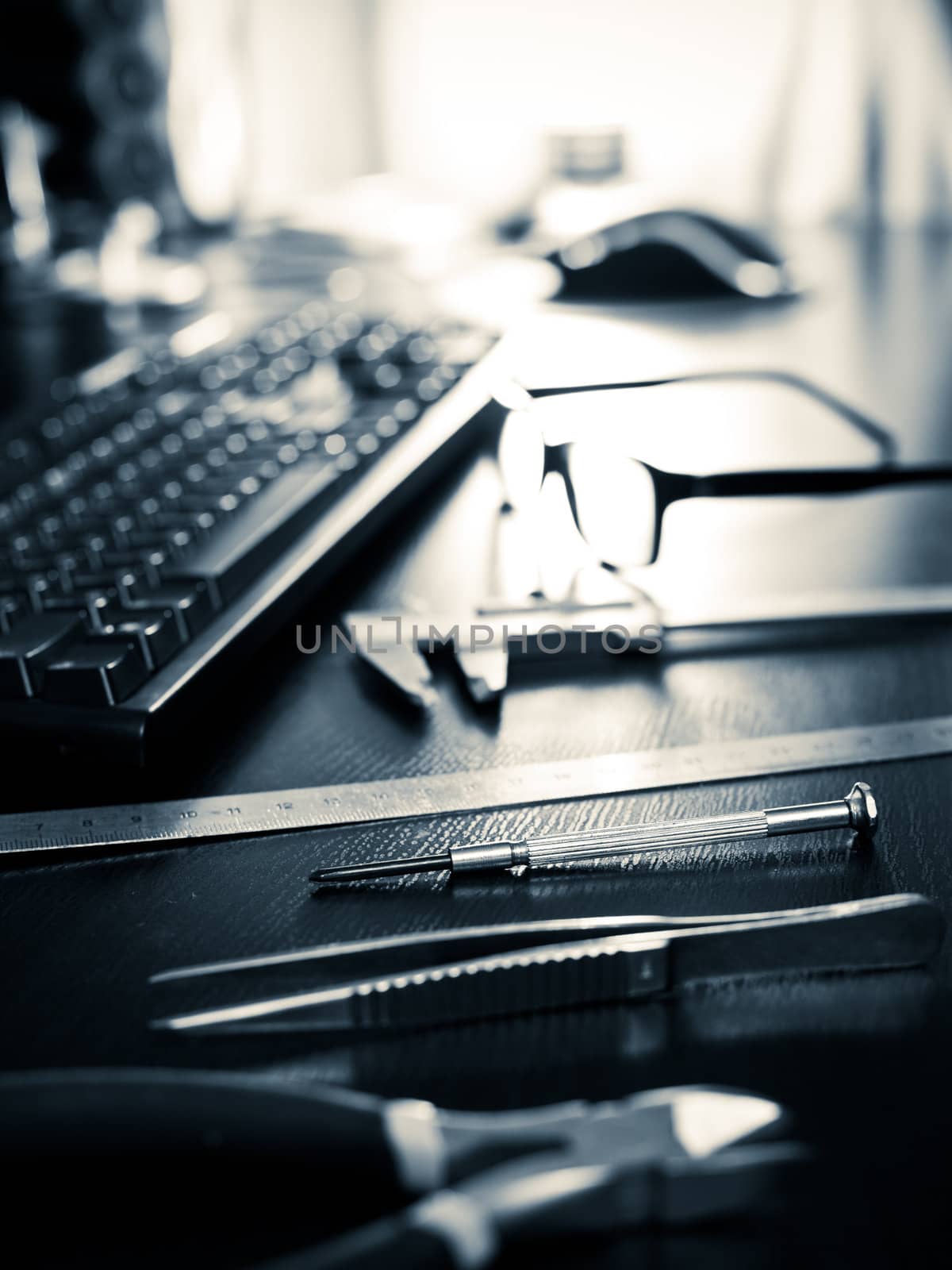 Screwdriver, pincers, ruler, caliper with keyboard and glasses on a table, very shallow DOF
