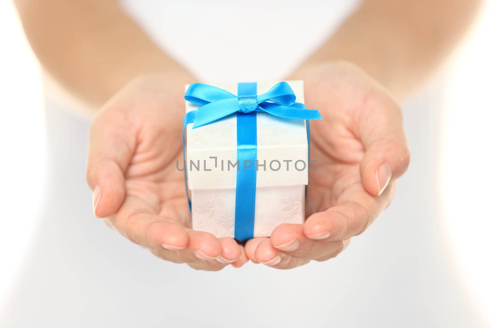 Decorative gift box tied with a turquoise ribbon and bow carefully cupped in female hands as she gives a surprise present to a loved one
