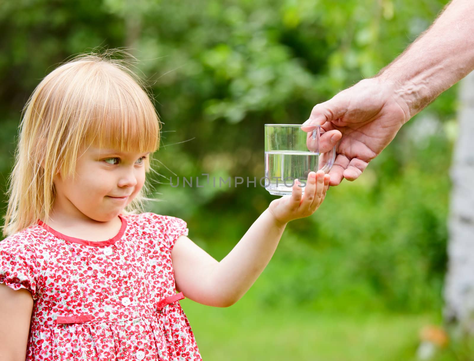 Adult giving mug of water to little girl outdoors