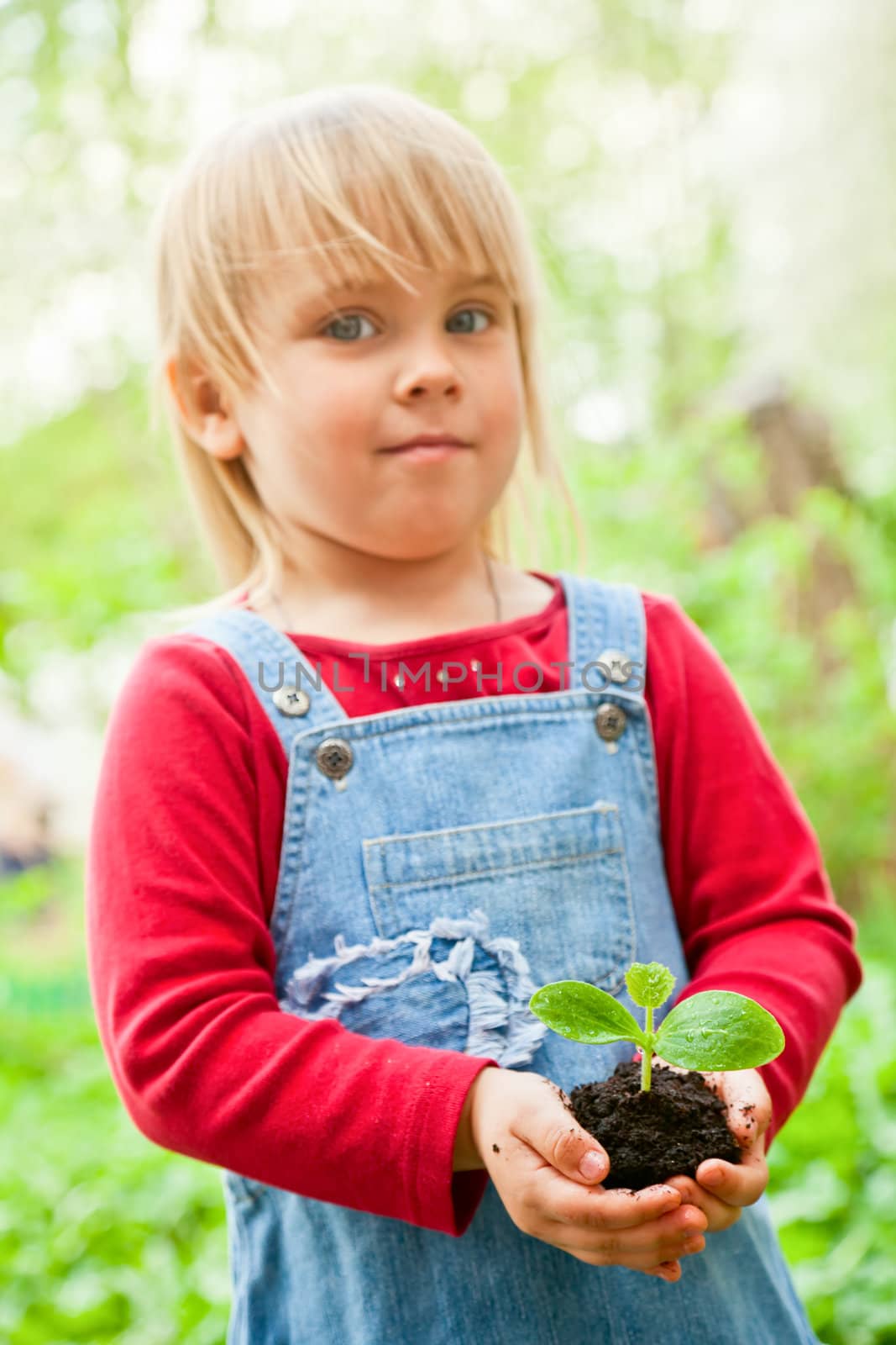 Blonde girl wearing red dress showing seeding with ground, focus on sprout