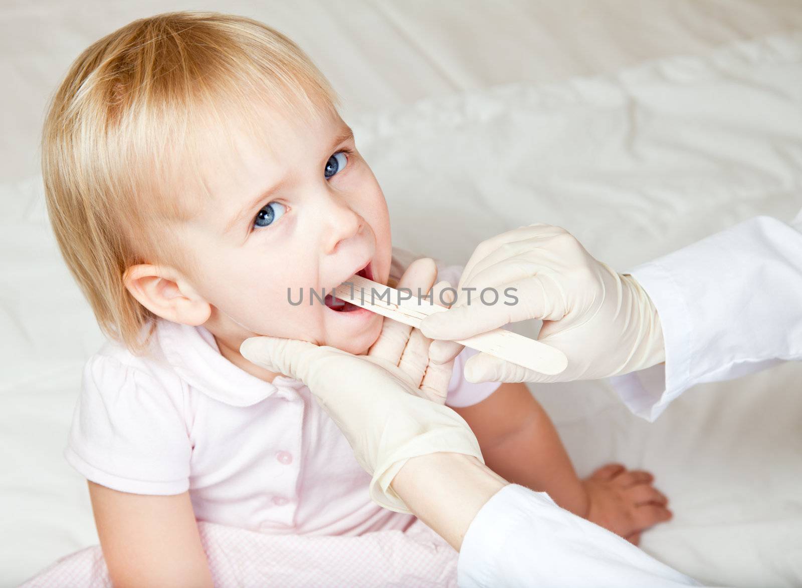 Pediatrician examining little girl's throat with tongue depressor