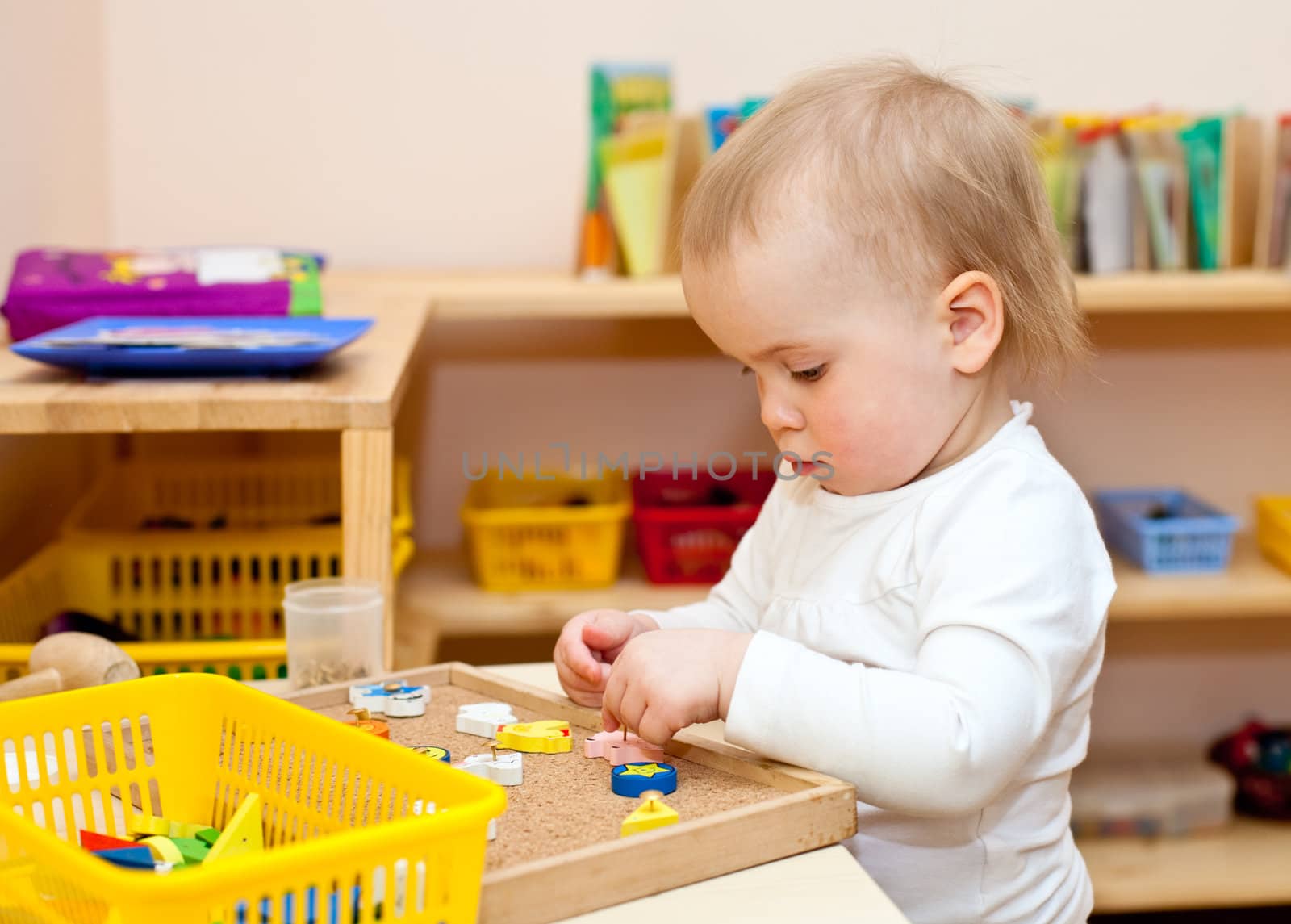 Little baby girl playing with wooden toys at nursery