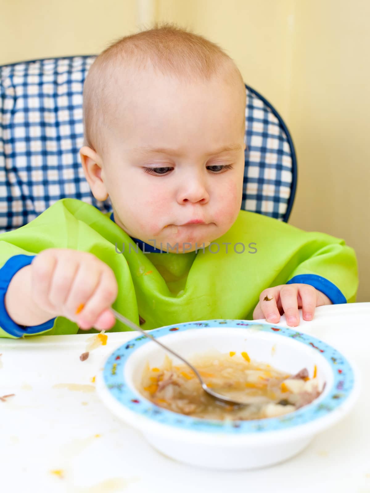 Little baby girl eating with spoon in a highchair