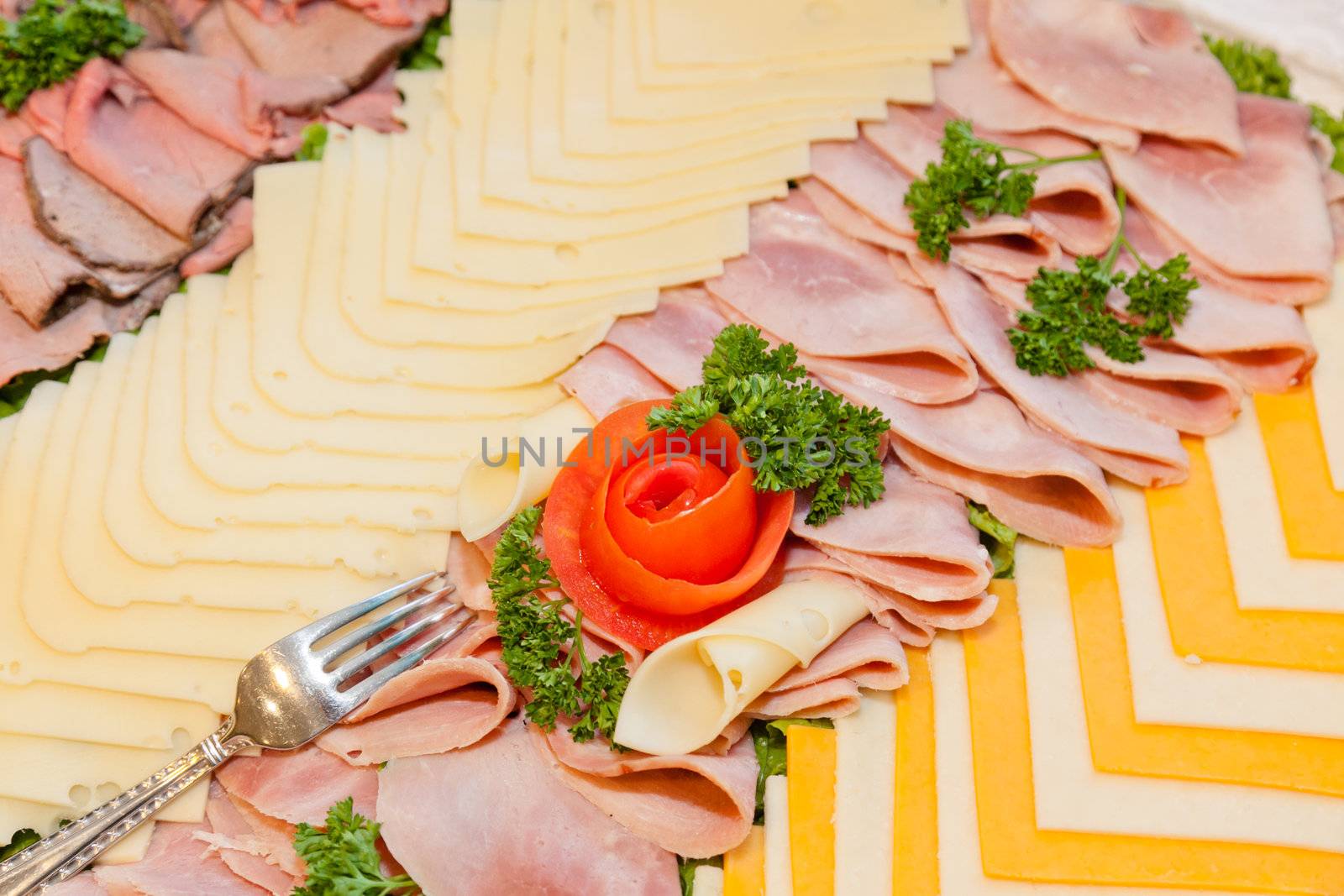 Party tray of assorted meats and cheeses with  flower made of tomato in the middle.