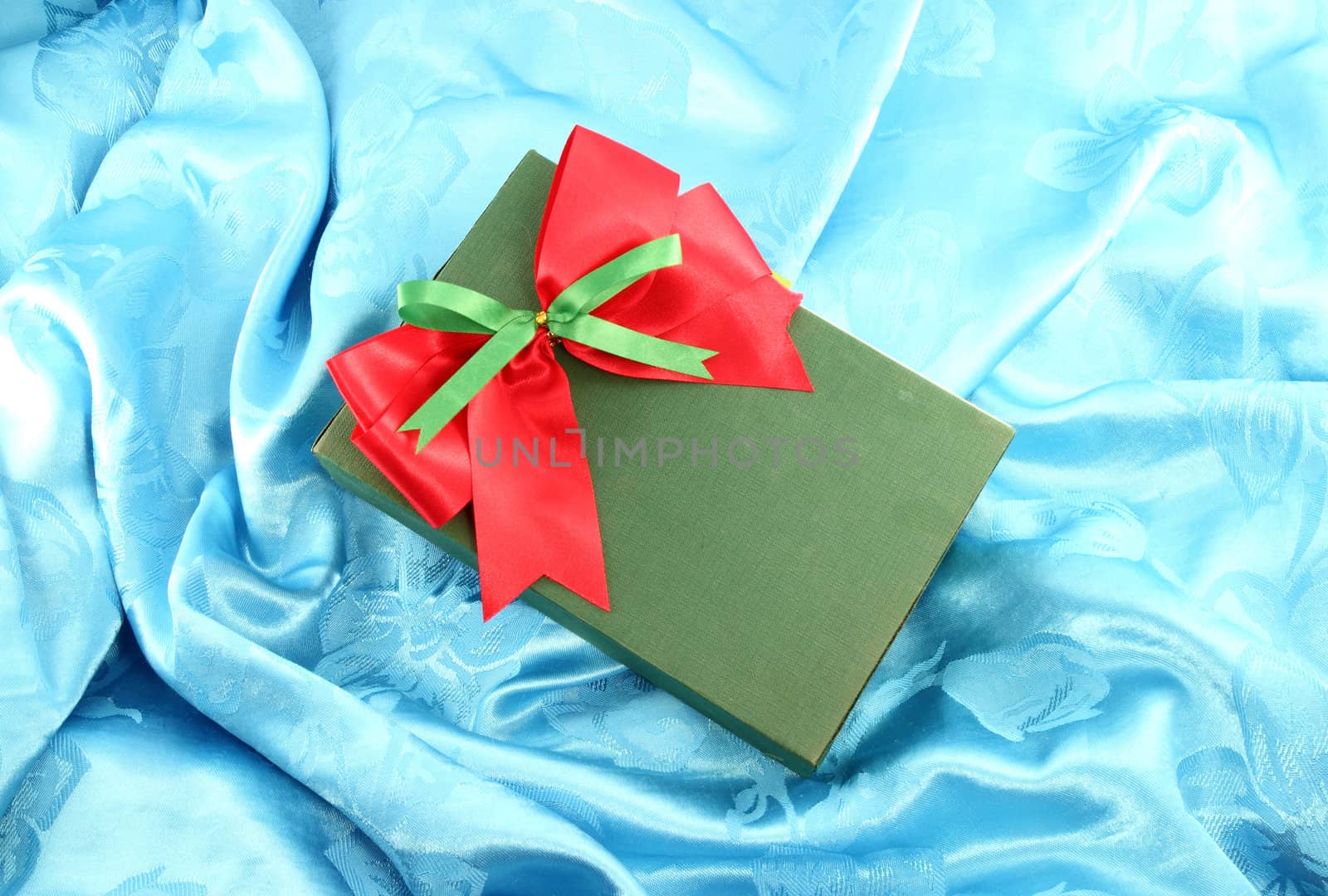 green gift box with red ribbon on blue satin
