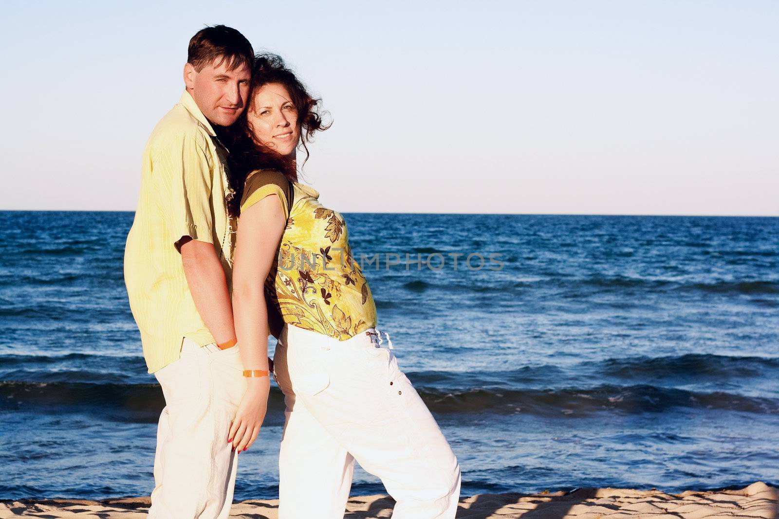 A young man and woman embracing as a romantic couple standing in the sea on a beach with a blue sky