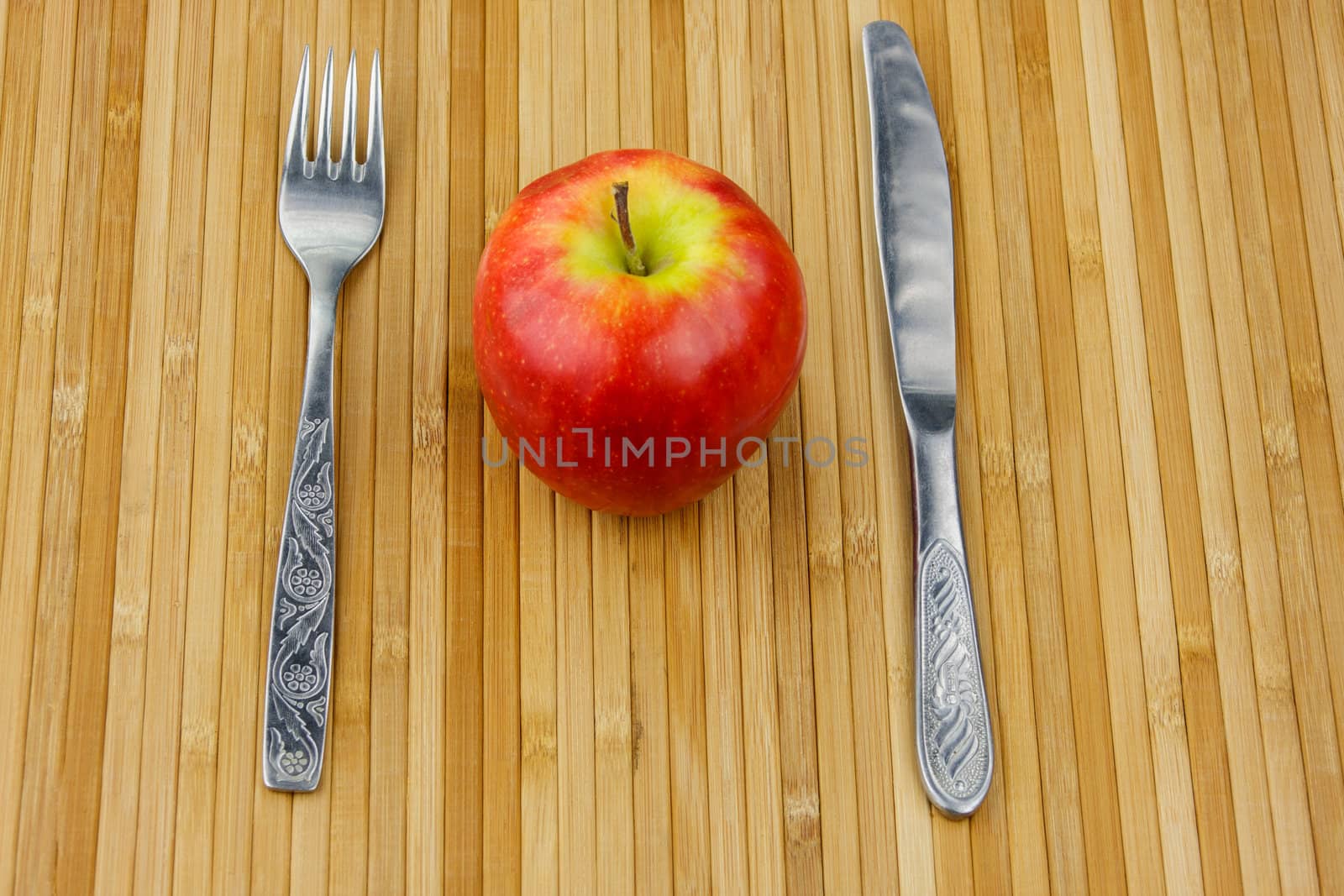 red apple lying on a bamboo napkin with cutlery