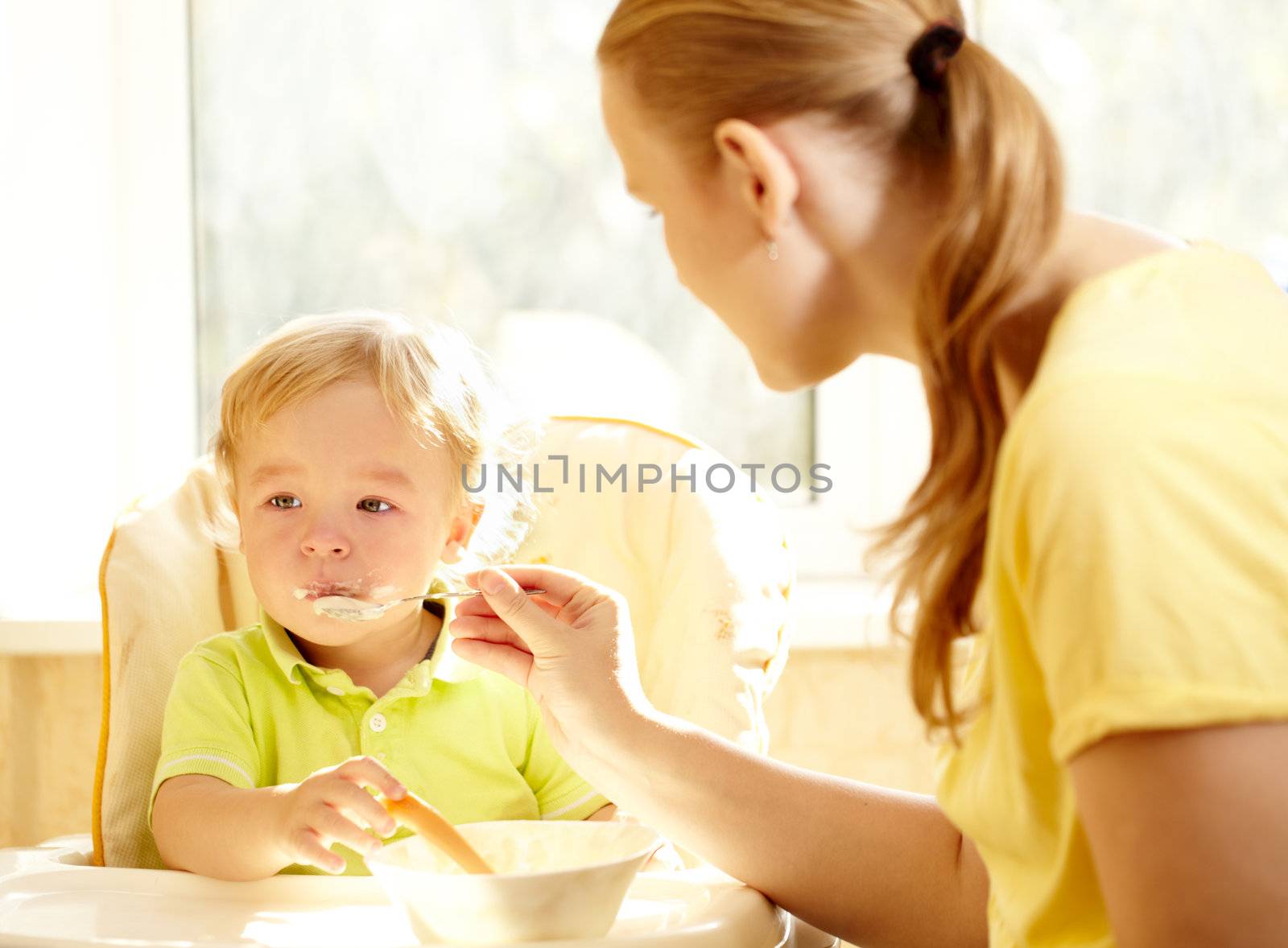 Young mother is feeding her two year old boy with porridge.