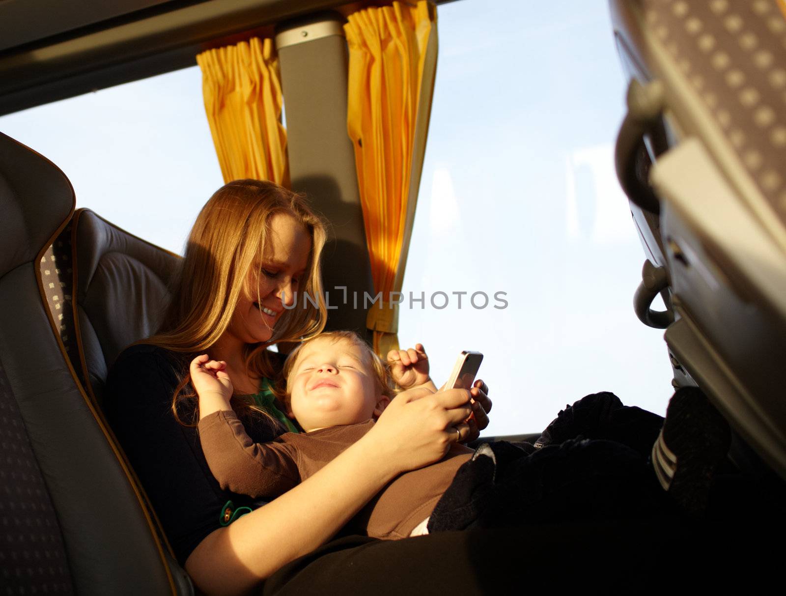 Young mother is playing games on the phone with her son, while travelling by bus. Boy is smiling and screwing up his eyes.