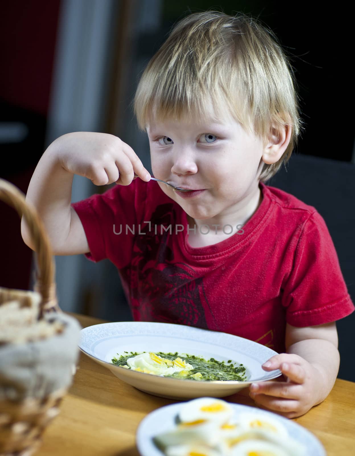 Young caucasian boy eating spinach soup with egg