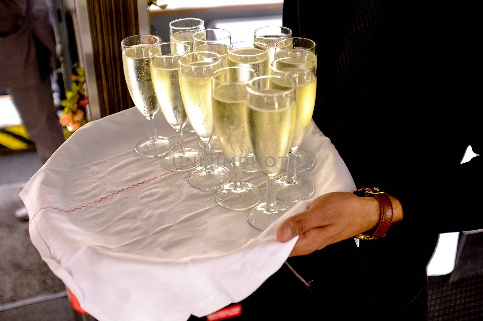 Cropped image of a man carrying champagne glasses and walking around. Offering same to guests.