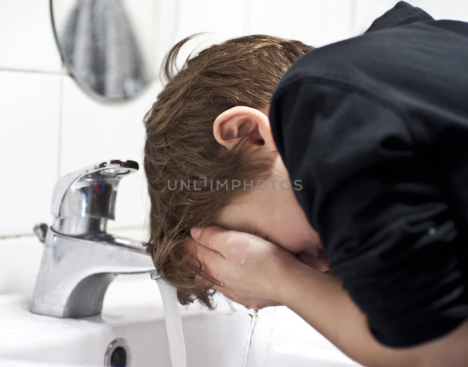 Young boy in domestic bathroom washing his face with water