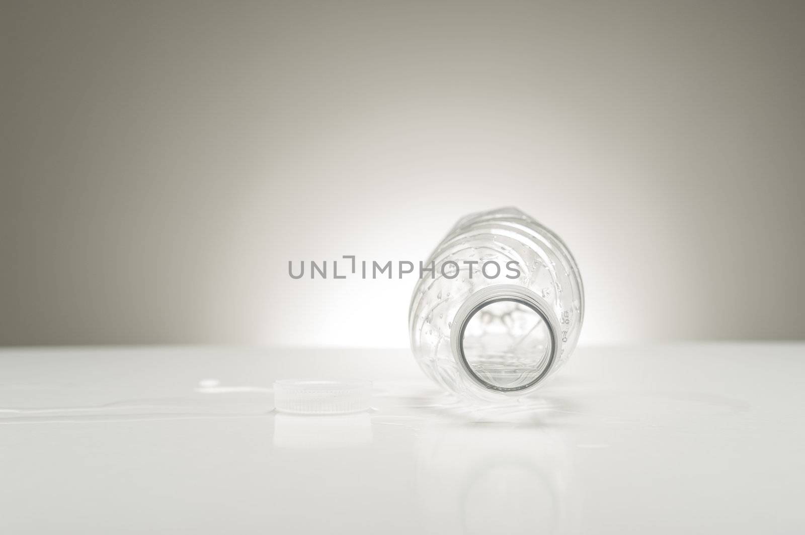Studio shot looking down the neck of an empty water bottle, which is laying on a white surface with a neutral background behind