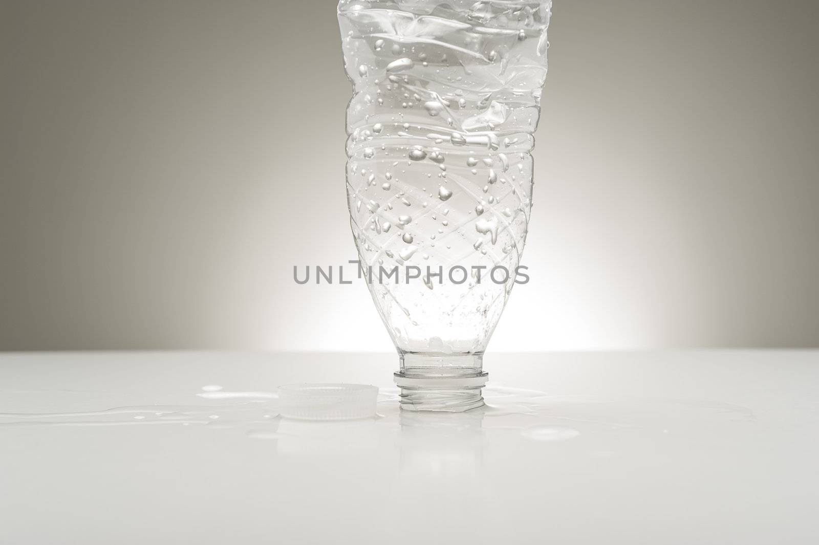 Studio shot of a plastic bottled covered in water droplets upended on a countertop surrounded by spillage conceptual of pure bure bottled water