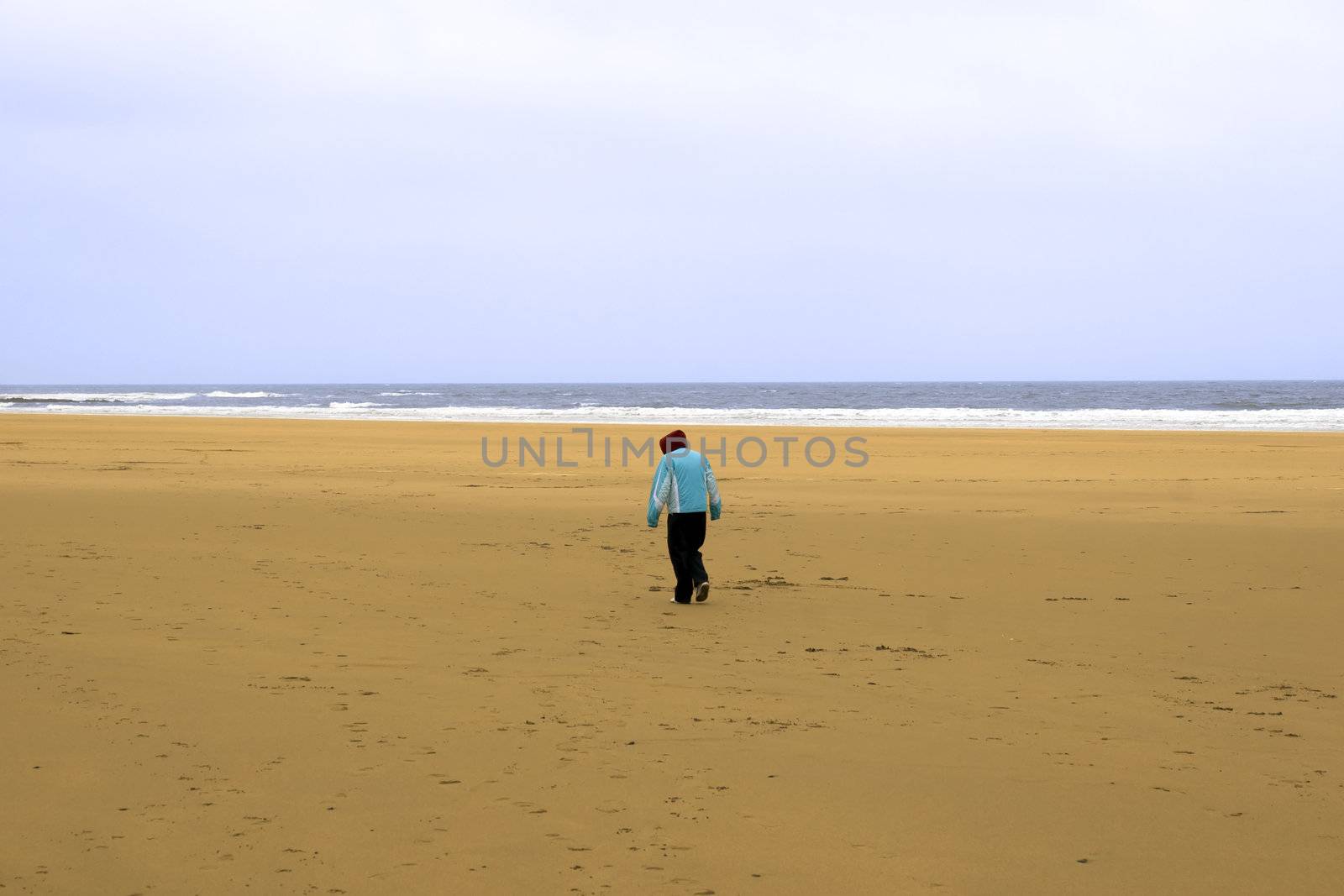 lone girl walking a beach against the cold wind by morrbyte