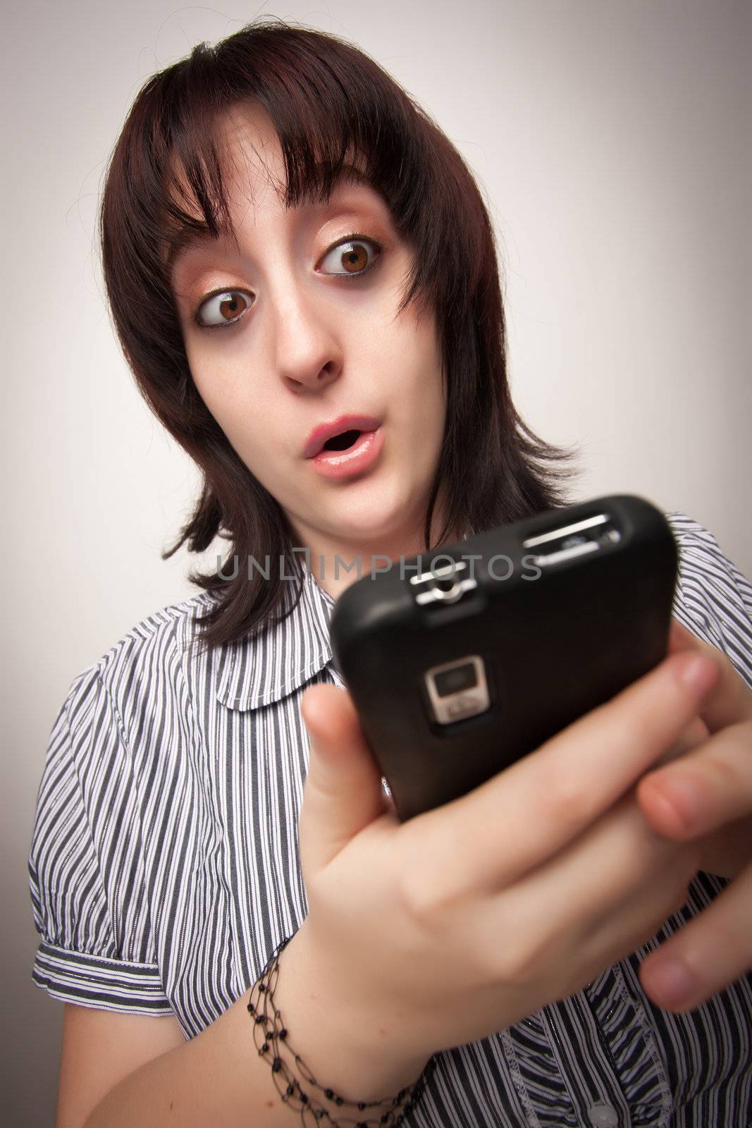 Stunned Brunette Woman Using Cell Phone on a Grey Background.