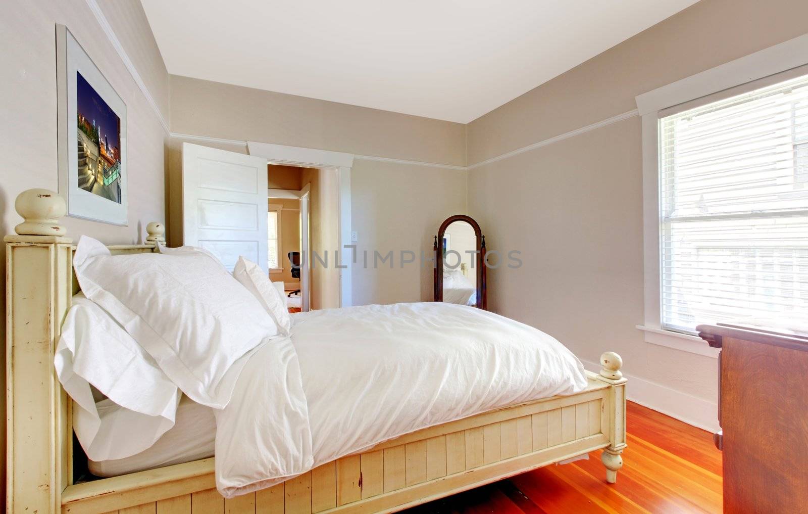 Bright bedroom with white bed, beige walls and hardwood floor.