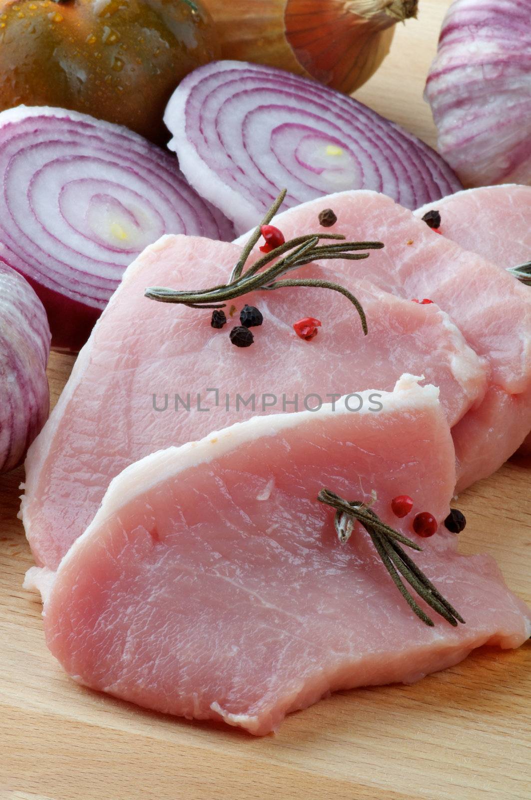 Arrangement of Raw Pork Loin Chops with Rosemary, Peppercorn and Onions on Wood Cutting Board closeup
