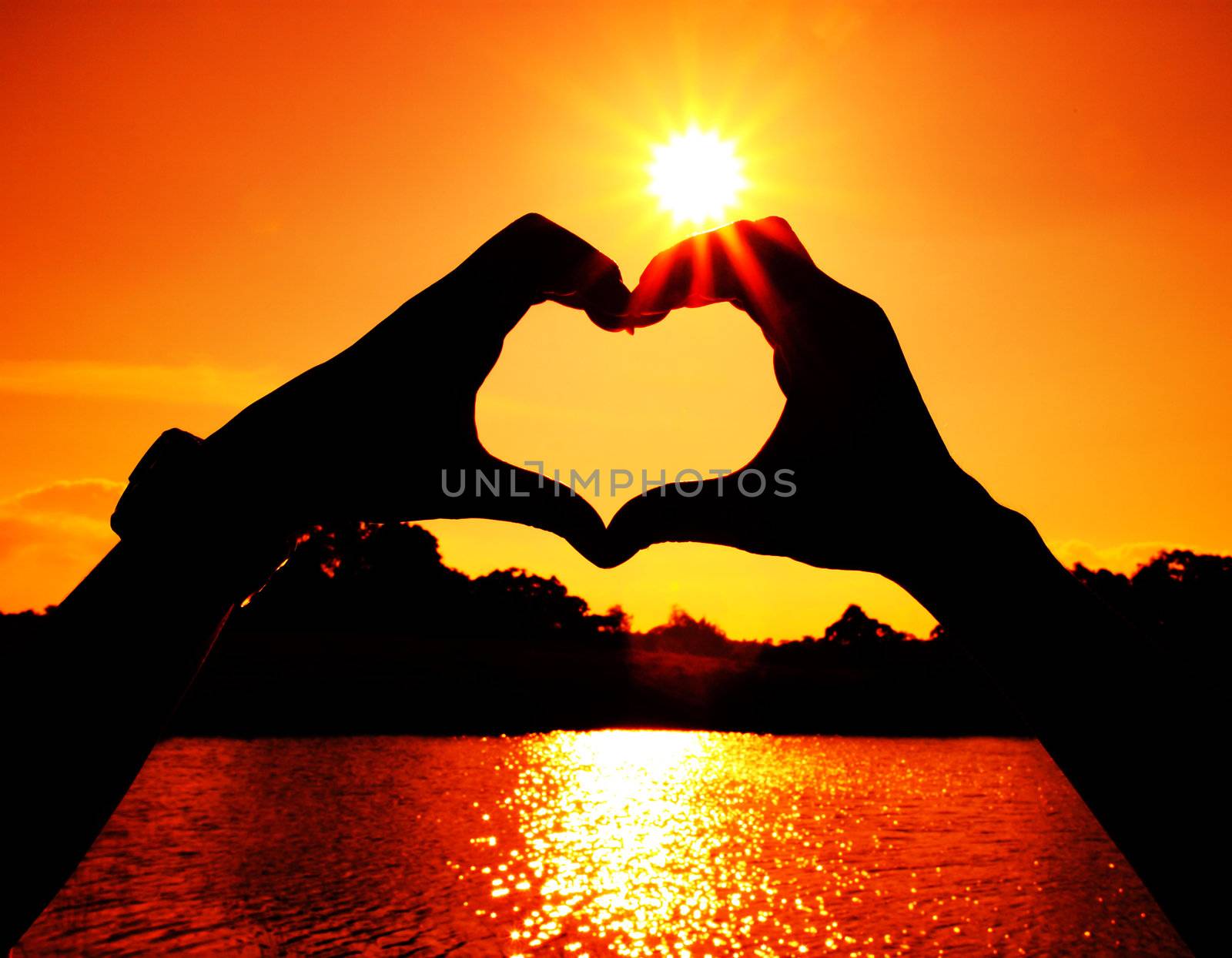 heart shape made with man and woman hands at the sun