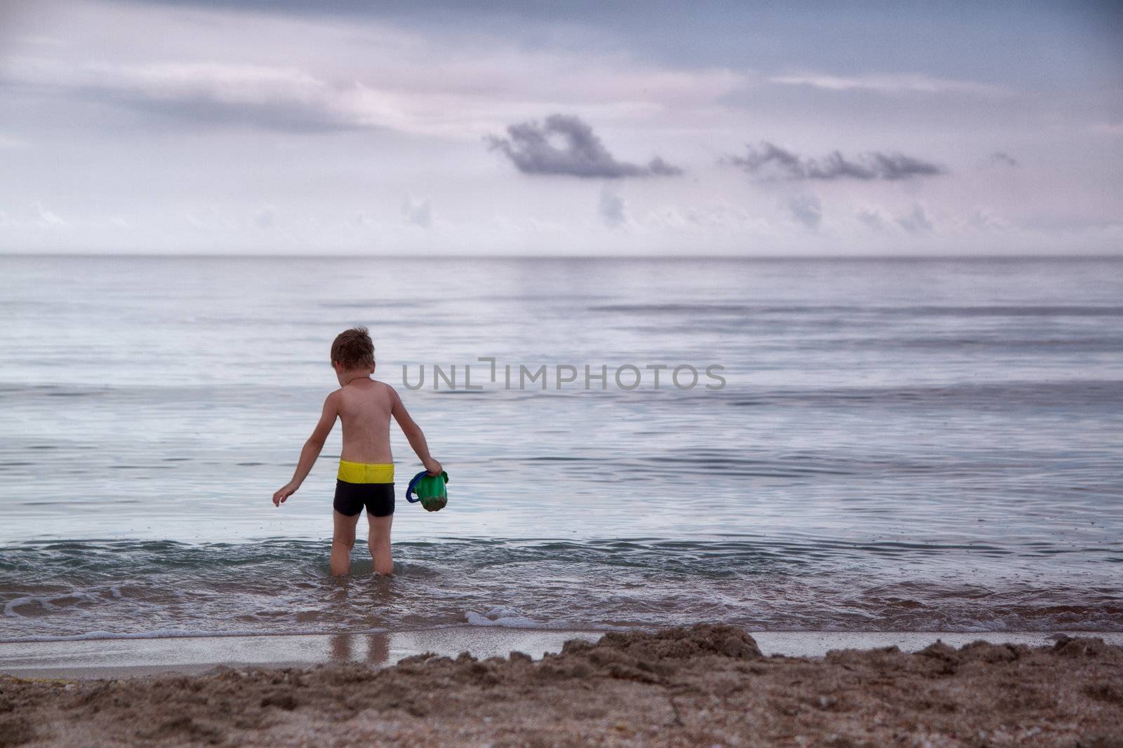 boy walks into cold sea water in a bucket to scoop up