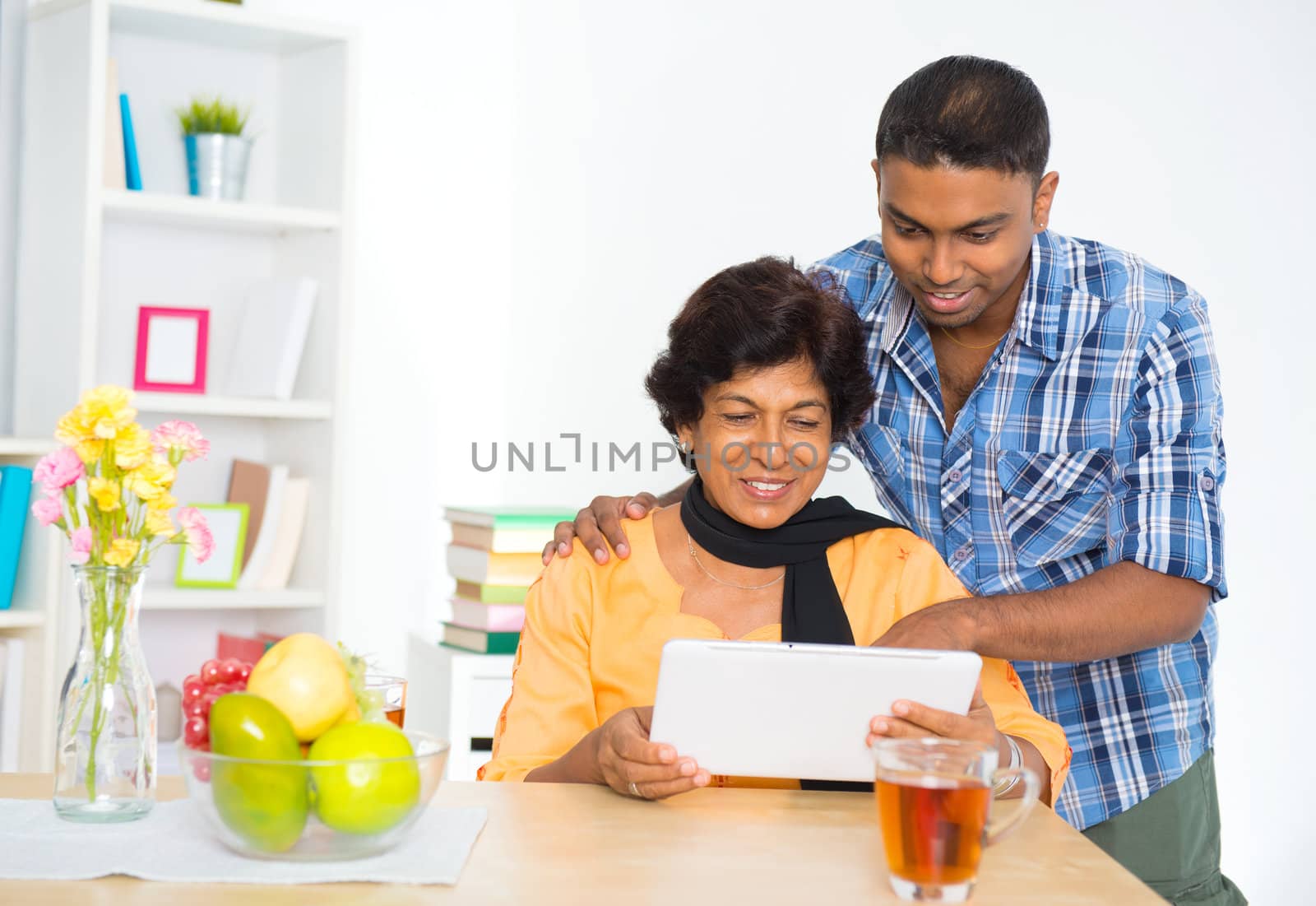 Mature 50s Indian woman and son using digital computer tablet at home
