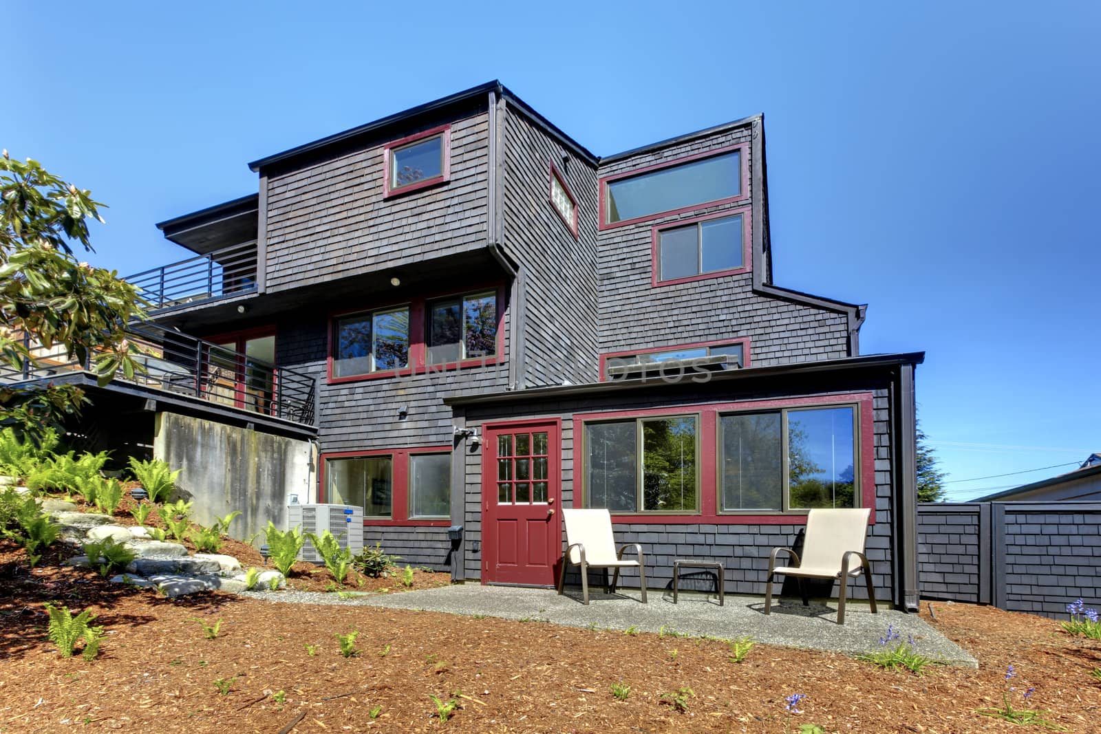 Black wooden modern house with spring backyard and two chairs.