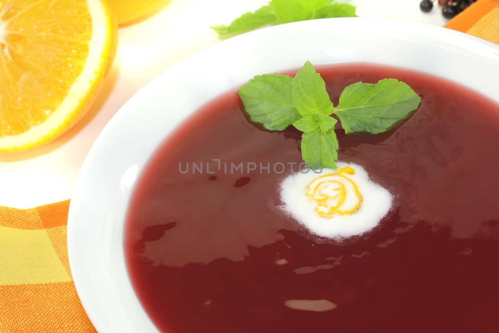 elderberry soup with dollop of whipped cream and mint on a light background