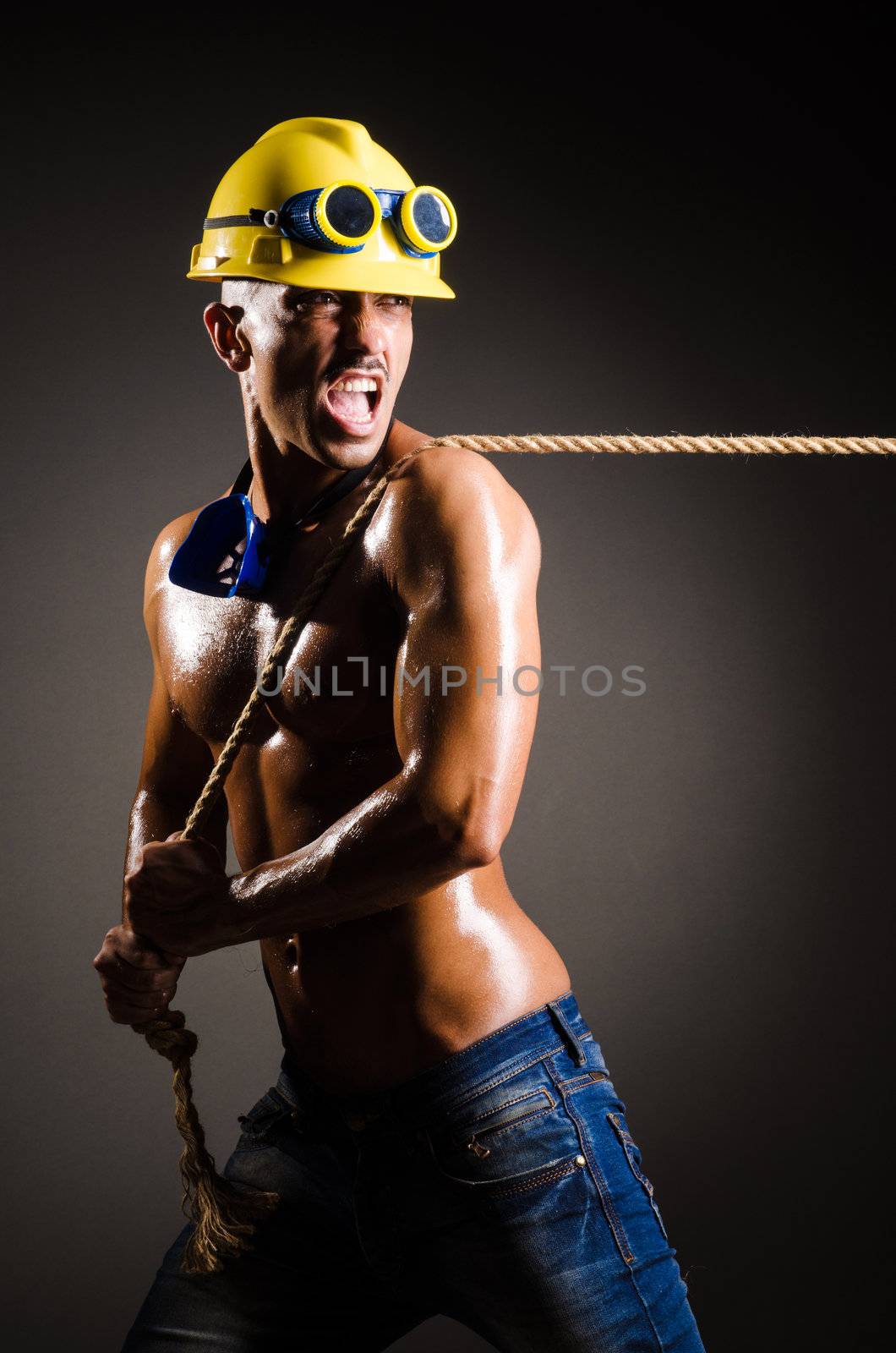 Nude builder pulling rope in darkness