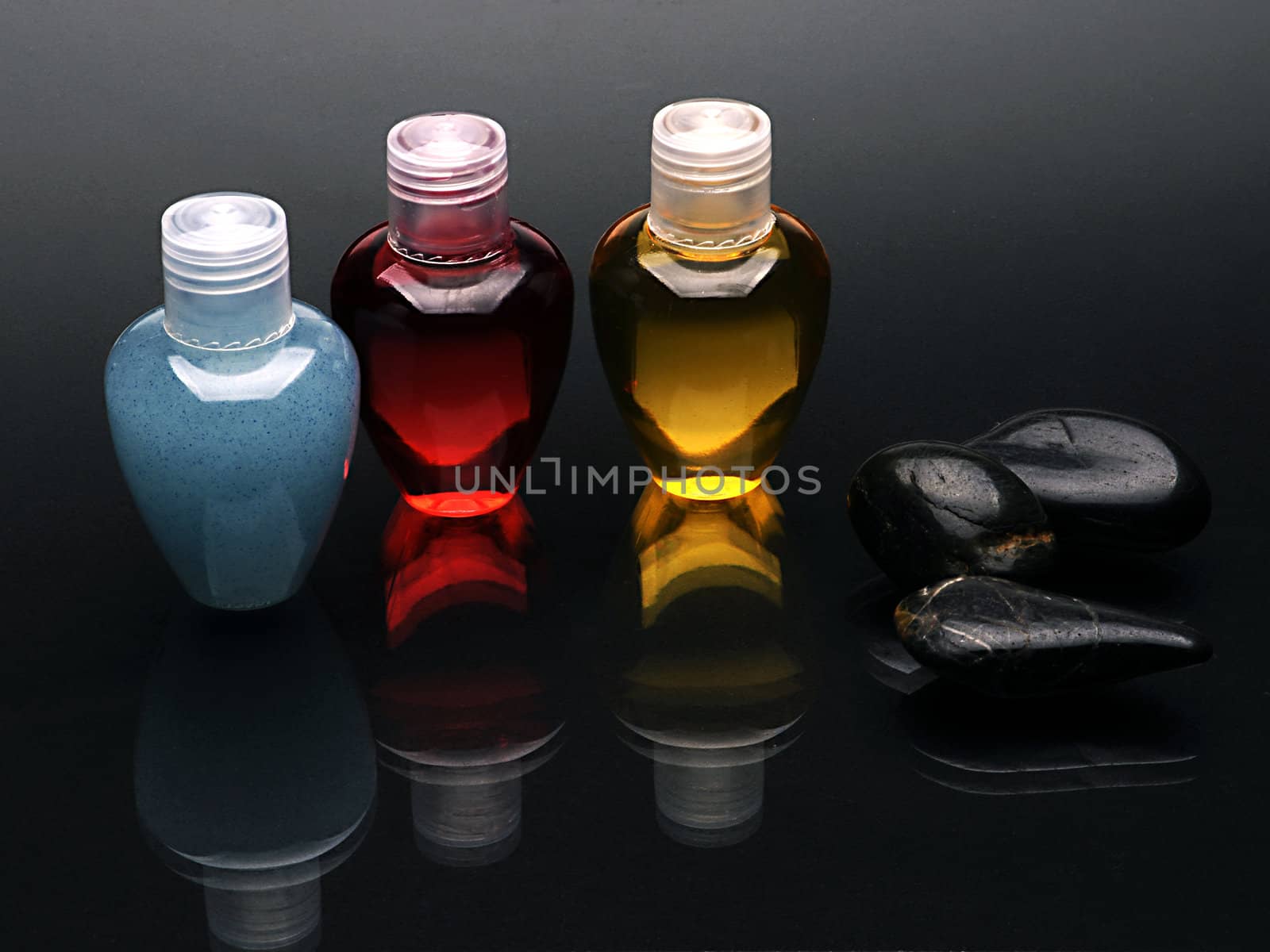 Colorful shampoo set and stones on reflected black surface