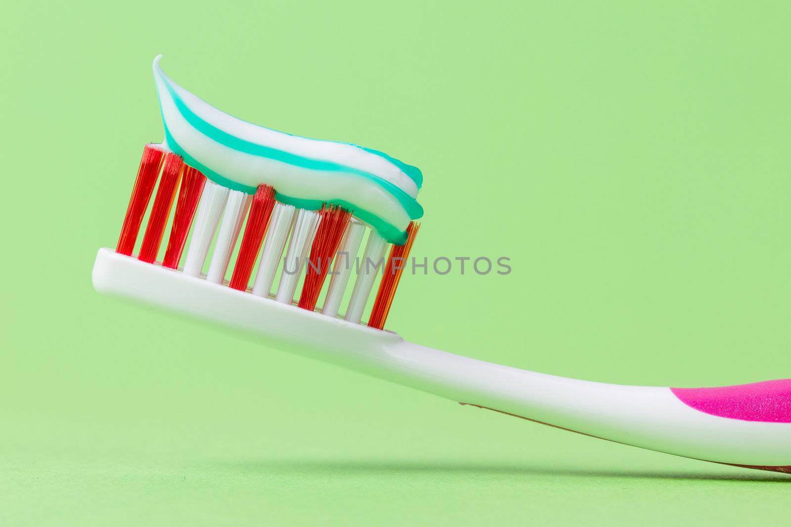 A pink toothbrush with toothpaste on a green background