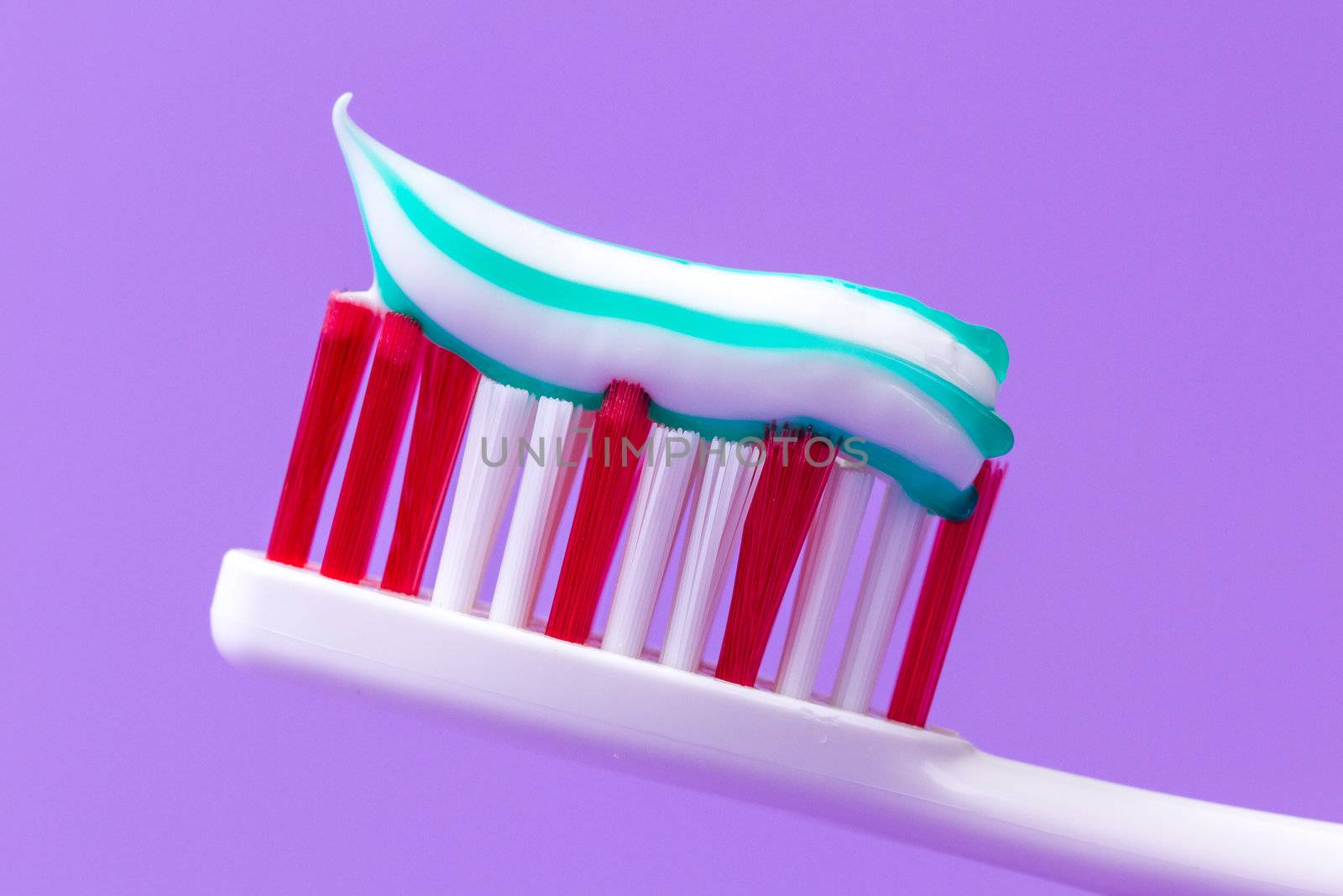 A pink toothbrush with toothpaste on a purple background