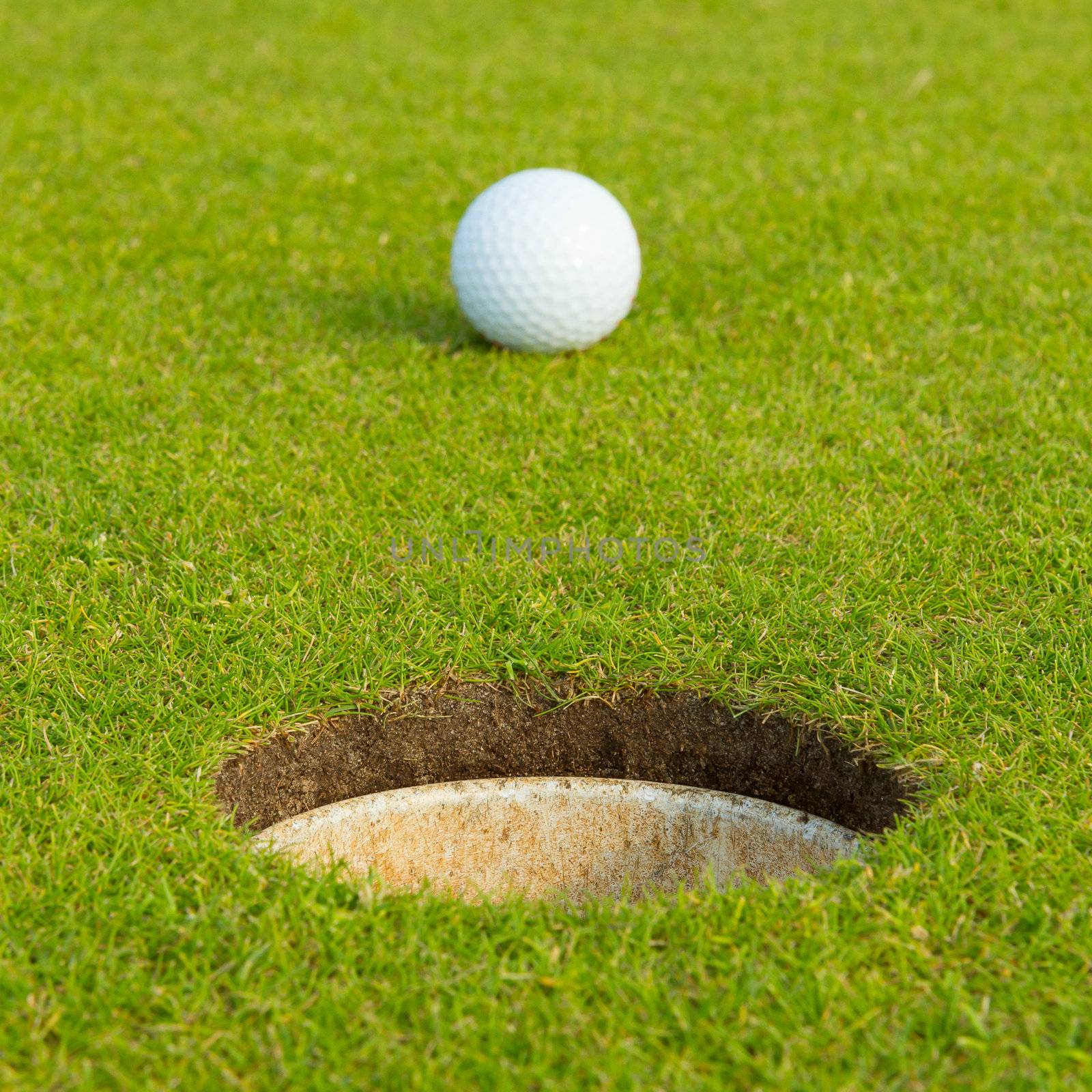 Golf ball on a green, in front of the hole, focus on the hole