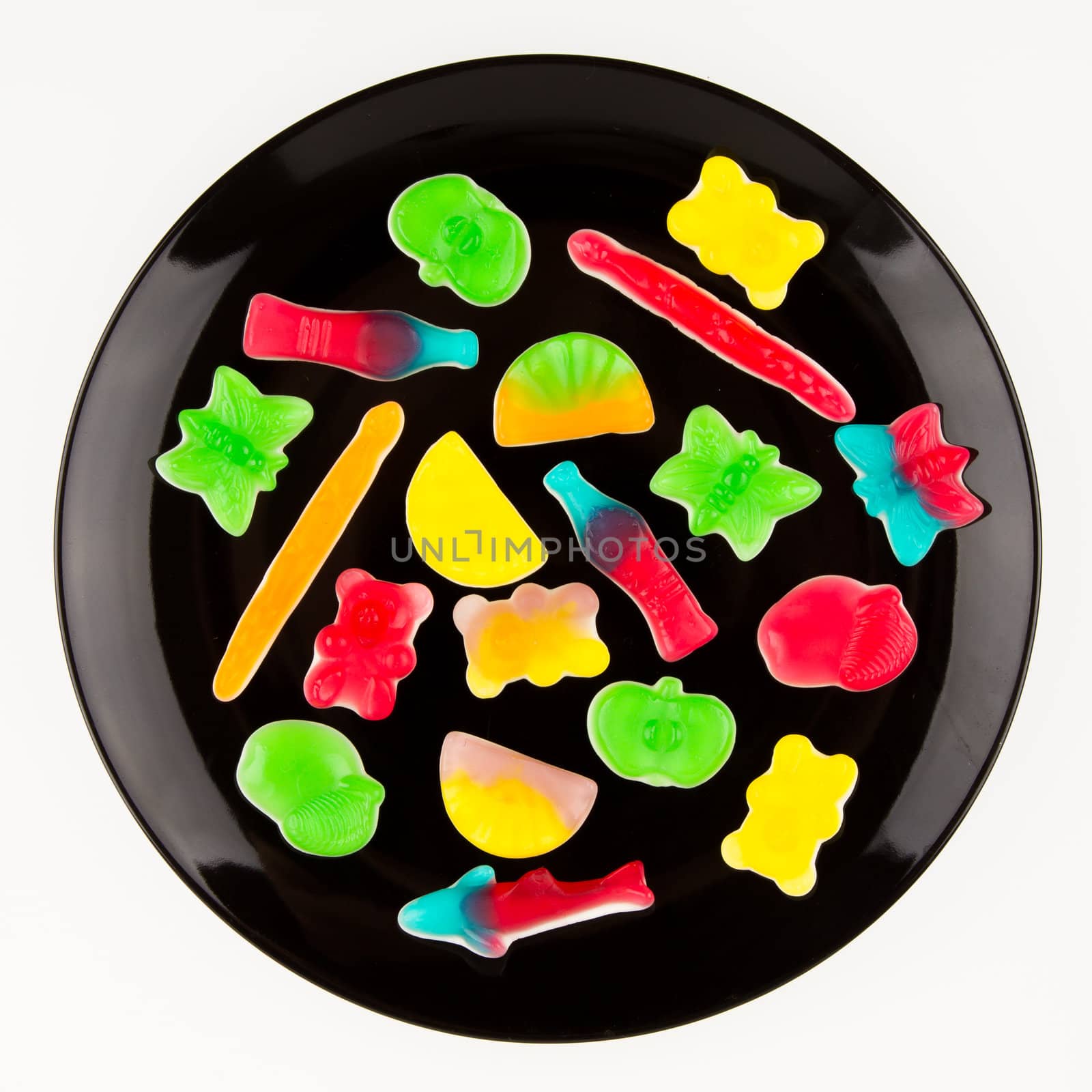 Colorful candies in many different shapes isolated on a black plate, isolated on white