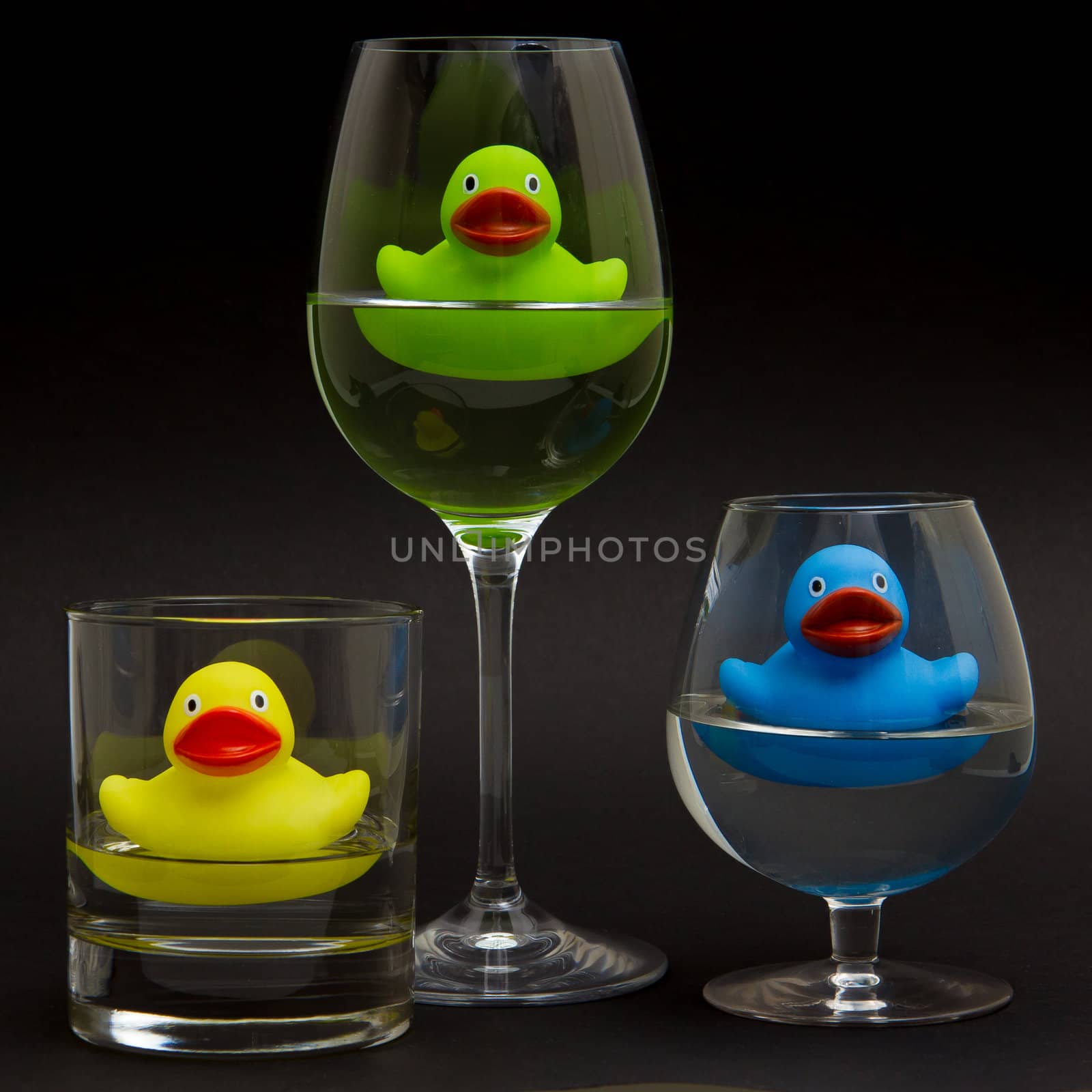 Green, yellow and blue rubber duck in different glasses on a dark background