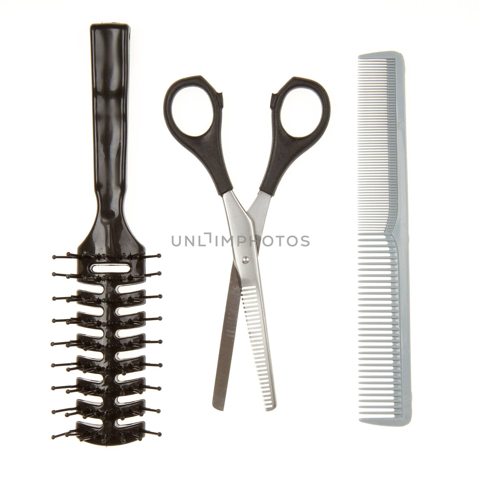 Close up of shiny silver hair cutting scissors or shears and black comb and a black brush isolated on white background